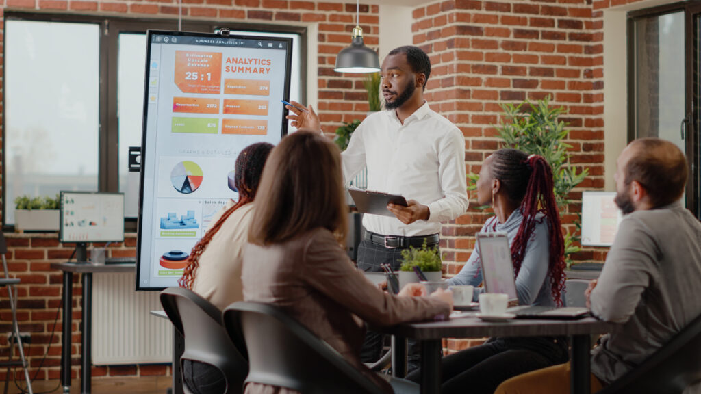 Company Employee Presenting Business Strategy With Charts Monitor Planning Project Workmates Analyzing Financial Statistics Display Working Together Company Development 1024x576